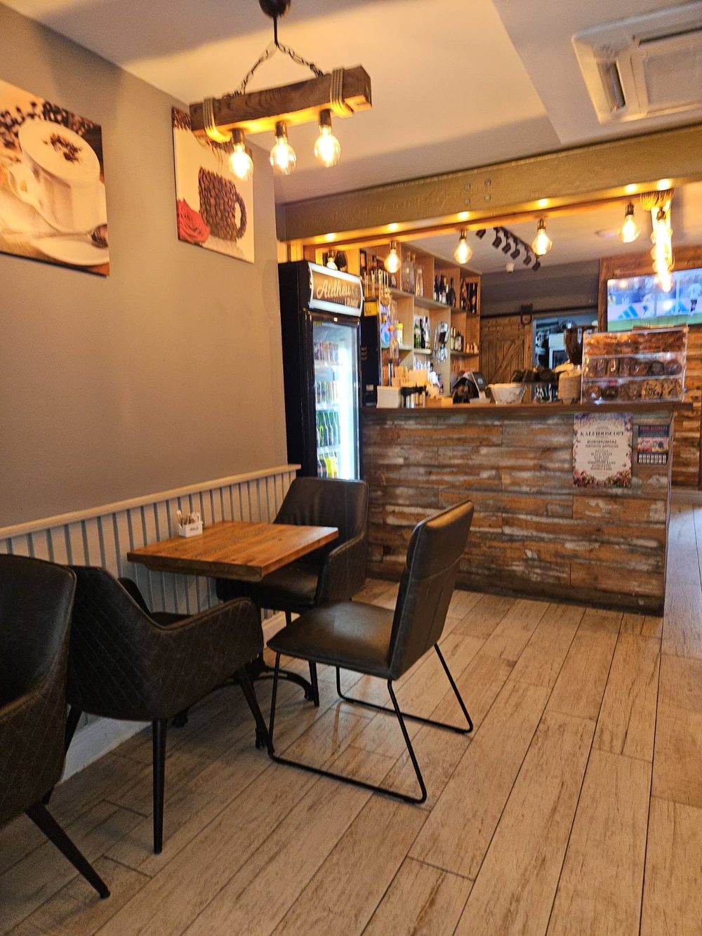 The service counter and back bar lit by pendant bulbs, with a small table for two in the foreground