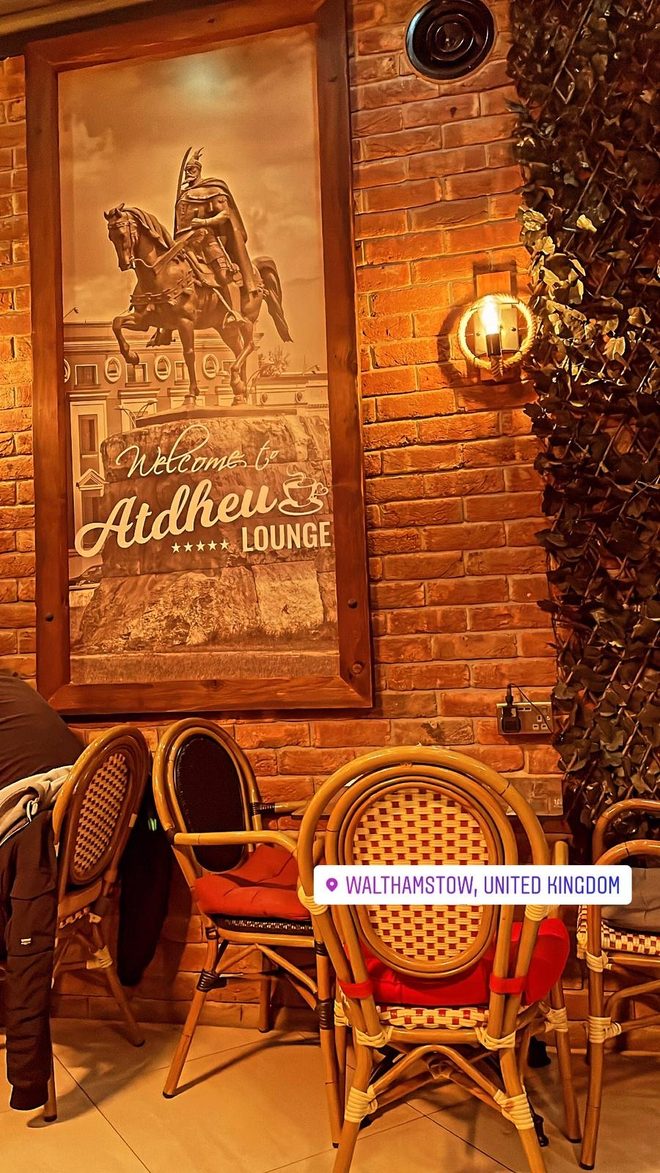 Outside seating with bistro chairs against a brick wall under a warm lamp (cropped to exclude the poster)