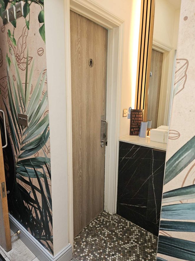 Corridor with a tropical leaf mural, a wooden door and a black marble washbasin