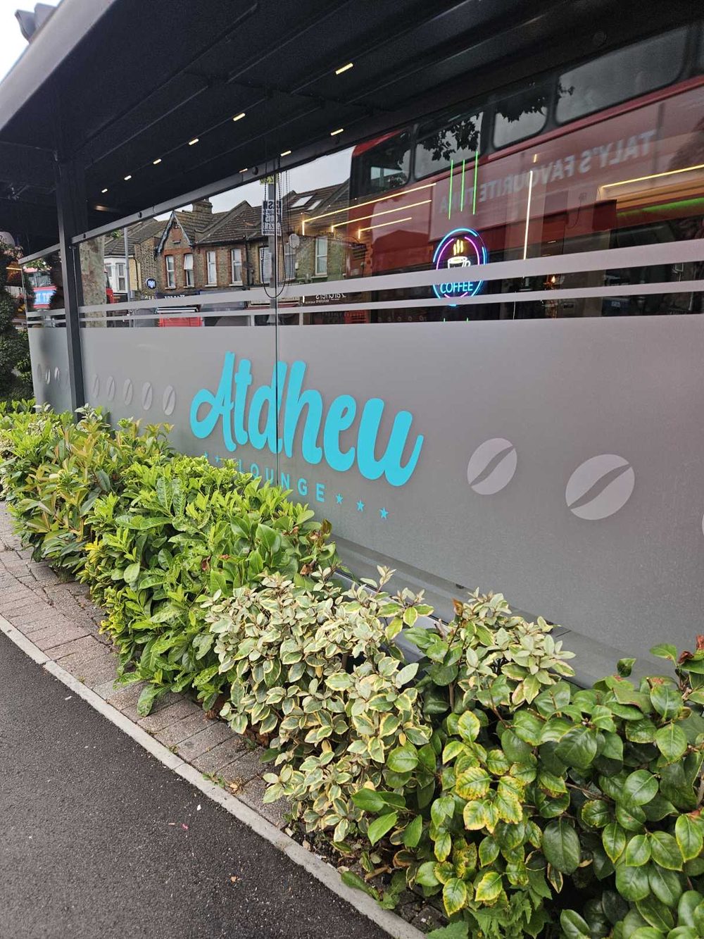 The Atdheu Caffe frontage on Hoe Street, grey facade with a planted bed of shrubs in front